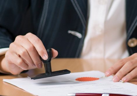 Young businesswoman (or notary public) sitting at the desk in office and stamping document