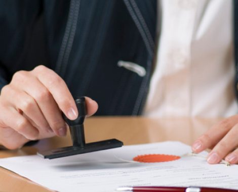 Young businesswoman (or notary public) sitting at the desk in office and stamping document